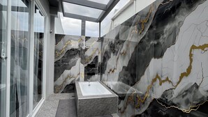 A modern bathroom with a marble wall, a bathtub, and a glass shower enclosure. - Vibe & Stay - Staycation home near Tagaytay (Nasugbu)