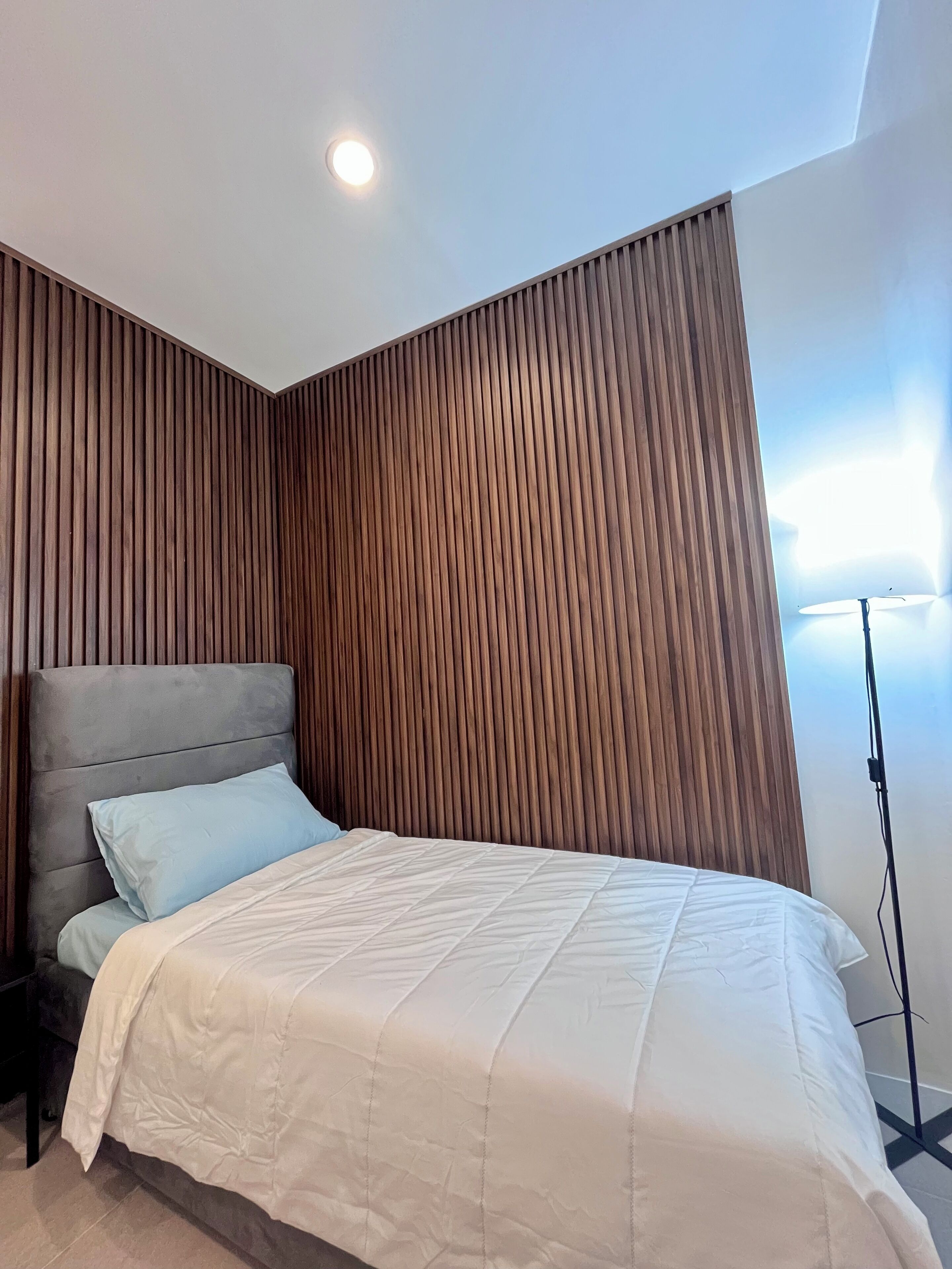 A modern bedroom with a bed, a headboard, and a wooden wall panel.