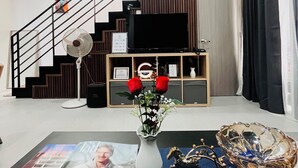 A modern living room with a staircase, a flat-screen TV, a vase with red roses, and a magazine on a coffee table. - Vibe & Stay - Staycation home near Tagaytay (Nasugbu)