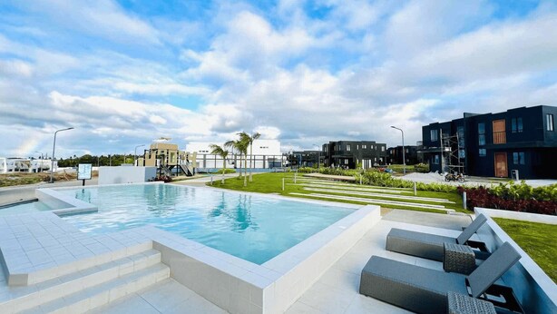 A modern outdoor pool area with a clear sky, a well-maintained lawn, and contemporary buildings in the background. - Vibe & Stay - Staycation home near Tagaytay (Nasugbu)