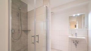 A modern bathroom with a glass-enclosed shower, a sink with a mirror above it, and tiled walls. - Landgasthof Hieren Mühle (Boppard)