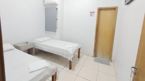 A small, clean room with two single beds, a bedside table, a wall-mounted air conditioner, and a door with a sign. - Hotel Oliveira 44 (Goiânia)
