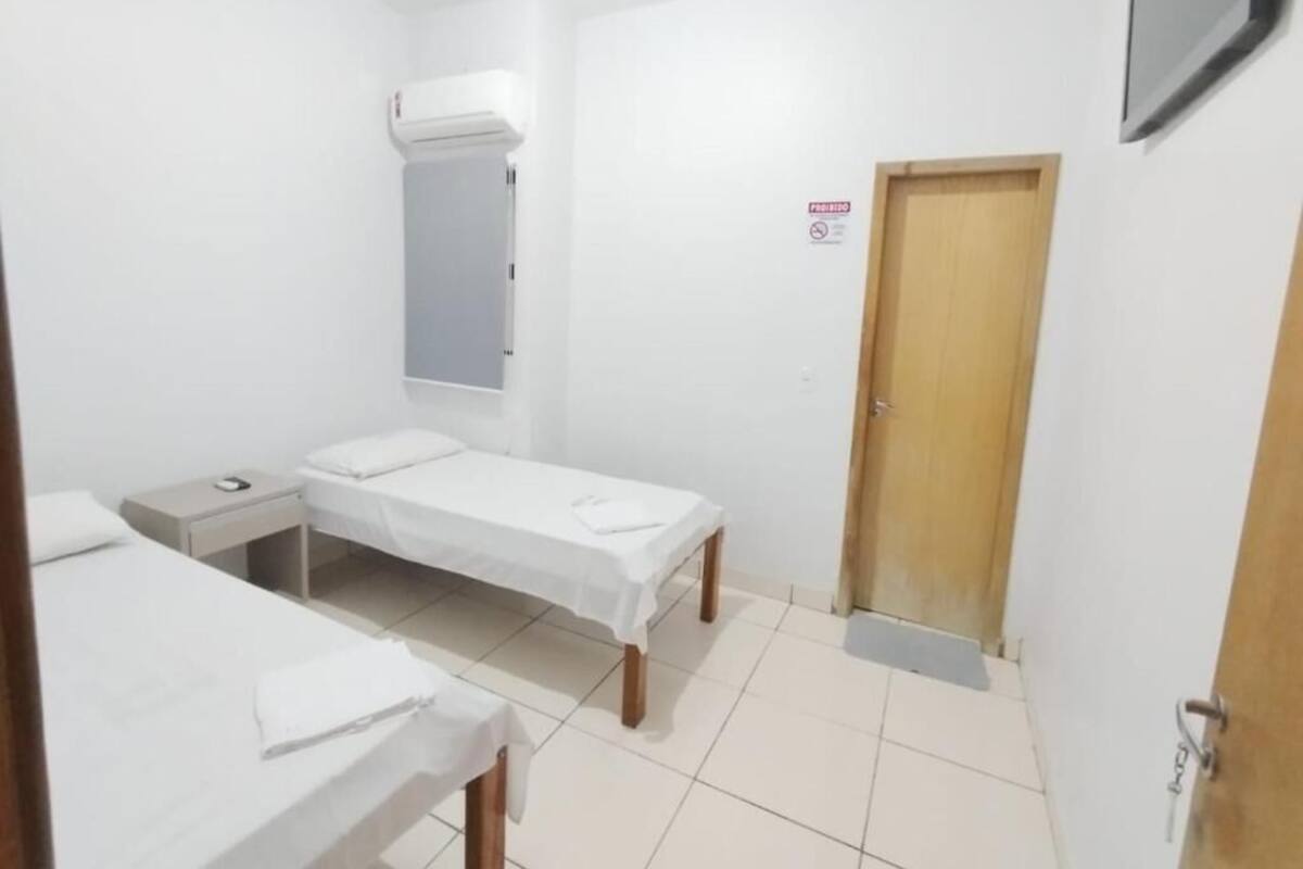 A small, clean room with two single beds, a bedside table, a wall-mounted air conditioner, and a door with a sign.