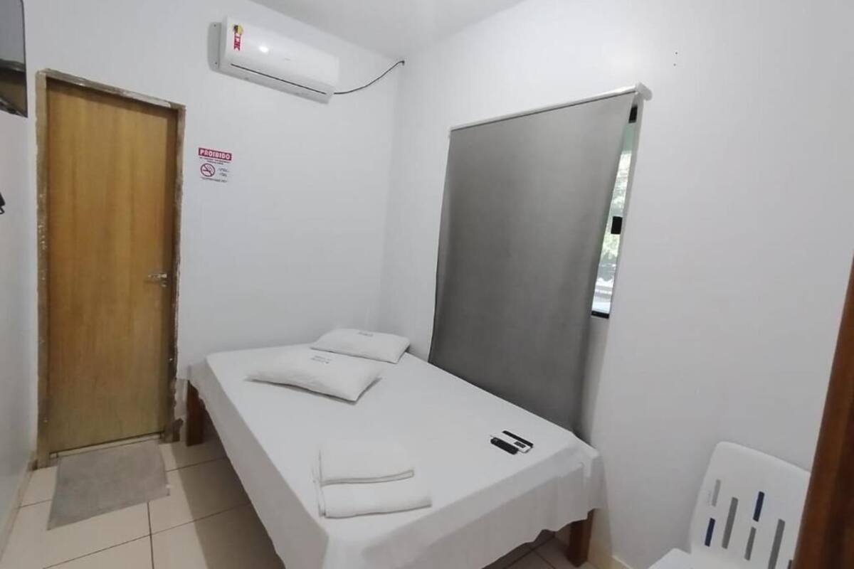 A small, clean room with a bed, a door, an air conditioning unit, and a window.