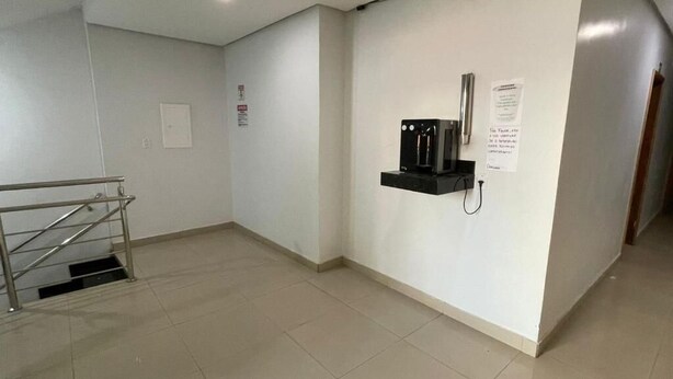 A clean, modern hallway with a coffee machine and a paper on the wall. - Hotel Oliveira 44 (Goiânia)