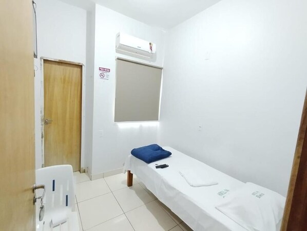 A small, clean room with a single bed, a window, and a door. - Hotel Oliveira 44 (Goiânia)