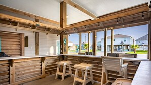 Un espacio al aire libre con bancos y mesas de madera, ventanas amplias y vistas al barrio.