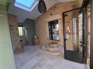 Een rustiek interieur met onbehandelde bakstenen muren, een dakraam, een stenen open haard en een moderne glazen deur.