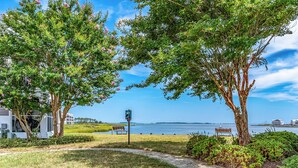 A pathway leading to a bench by a body of water, with a building and a sign in the background. - Bethany Bay Hideaway: Spacious, Modern 4 bed, 4 bath condo, water & wetland view (Ocean View)