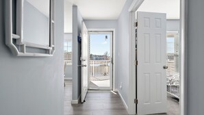A hallway with a wooden floor leading to a balcony with a white railing. - Bethany Bay Hideaway: Spacious, Modern 4 bed, 4 bath condo, water & wetland view (Ocean View)