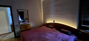 Ein Schlafzimmer mit Bett, Kommode, Spiegel und Fenster.