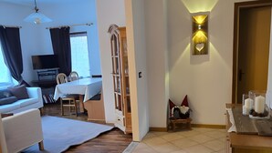Una sala de estar con sofá, una mesa de comedor, televisor y una lámpara de pared.