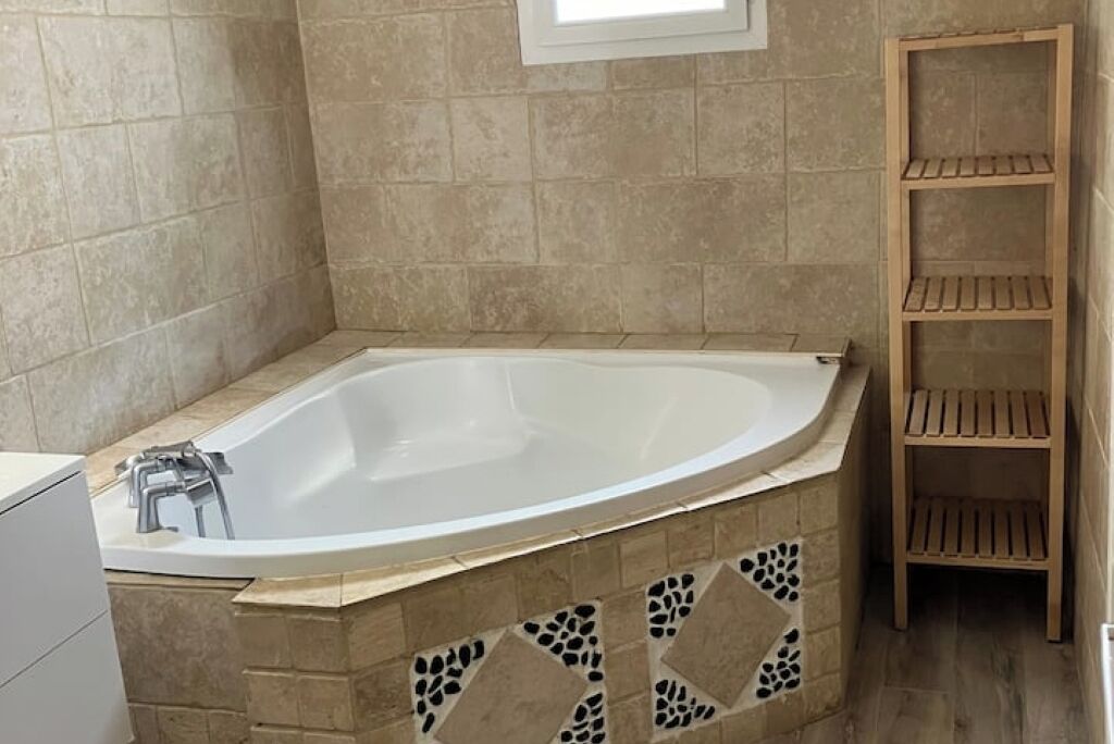 A bathroom with a freestanding bathtub, tiled walls, and a wooden shelf unit.