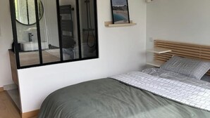A bedroom with a bed, a bedside table, a wall-mounted shelf with a picture, and a window with a view of a bathroom. - Superb air-conditioned villa with pool near Avignon (Tavel)