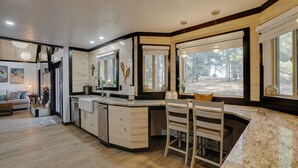 A modern kitchen with wooden cabinets, a granite countertop, and large windows offering a view of the outdoors. - Getaway in the trees (Angel Fire)