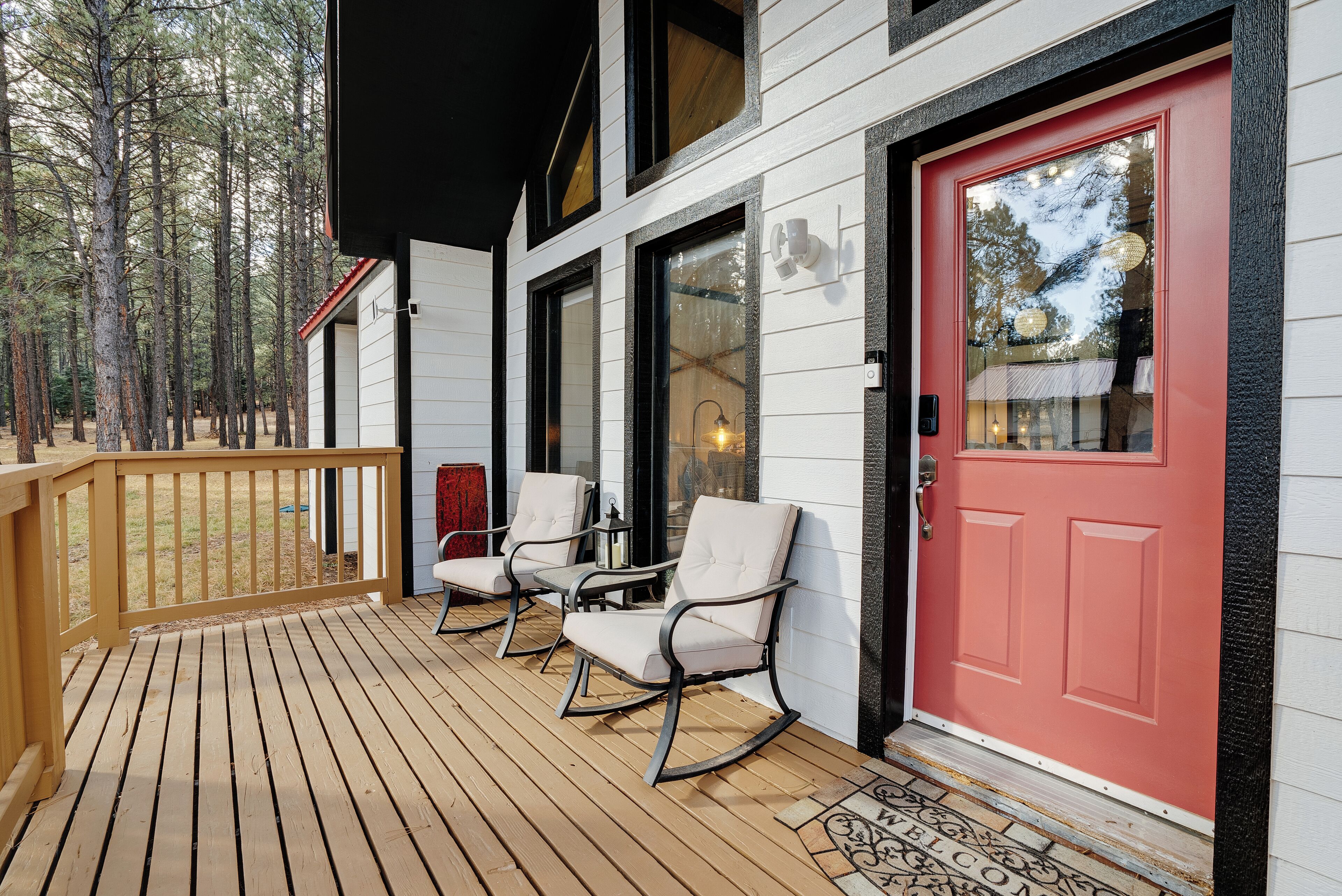 Une terrasse en bois avec des fauteuils à bascule et une porte rouge.