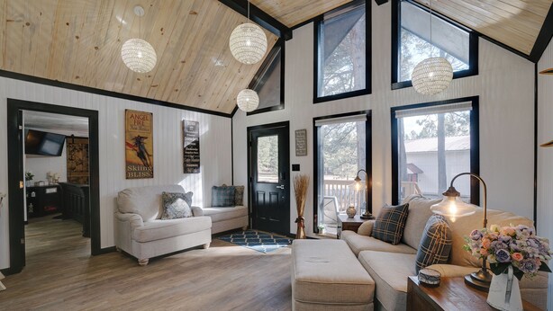 A spacious living room with a high ceiling, large windows, and a cozy fireplace. - Getaway in the trees (Angel Fire)