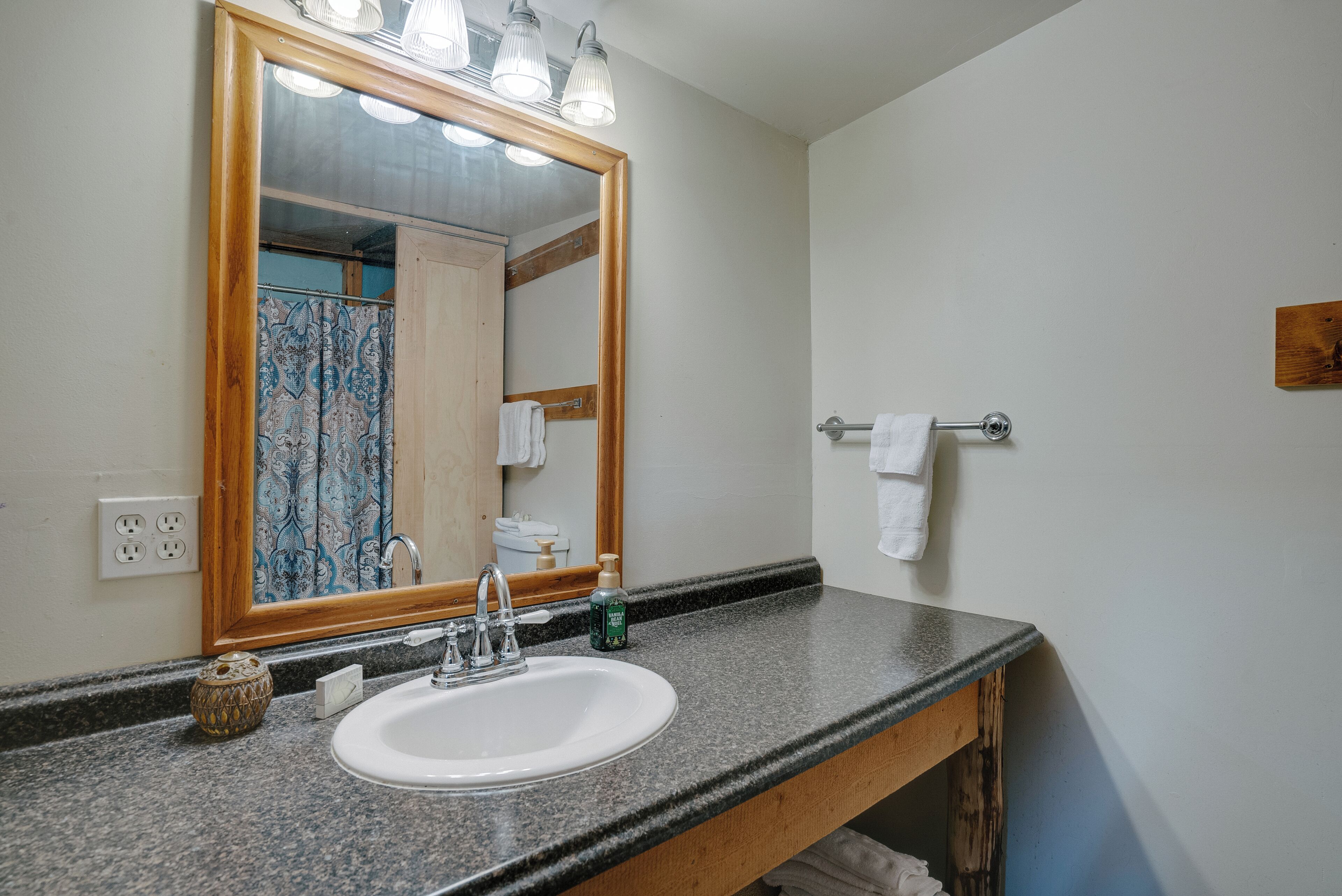 Une salle de bain dotée d’un comptoir en granit, d’un lavabo blanc, d’un miroir avec éclairage intégré et d’un porte-serviettes.