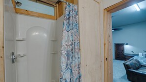 A room with a shower curtain, a wooden door, and a visible bed in the background. - Guest house escape in the trees (Angel Fire)