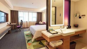 Une chambre d’hôtel comprenant un lit, un bureau, une chaise, un grand miroir et une salle de bain avec un lavabo et un porte-serviettes.