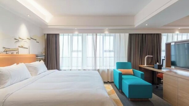 Une chambre d’hôtel avec un grand lit, un bureau avec une chaise, une télévision et une fenêtre avec des rideaux.