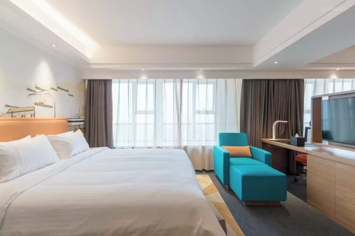 A hotel room with a large bed, a desk with a chair, a TV, and a window with curtains.