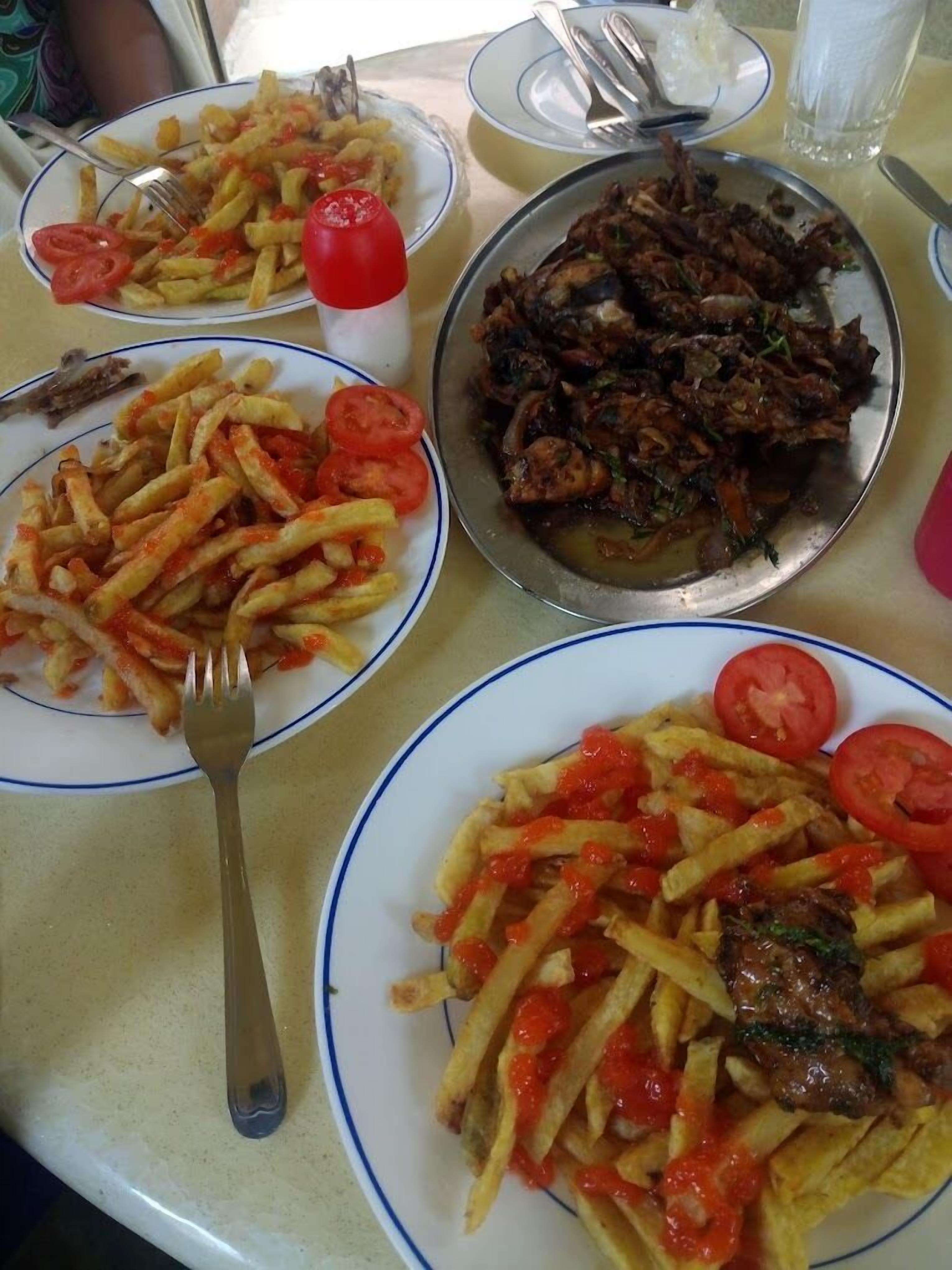 A table with four plates of food, including fries and a meat dish, and a fork on one plate.