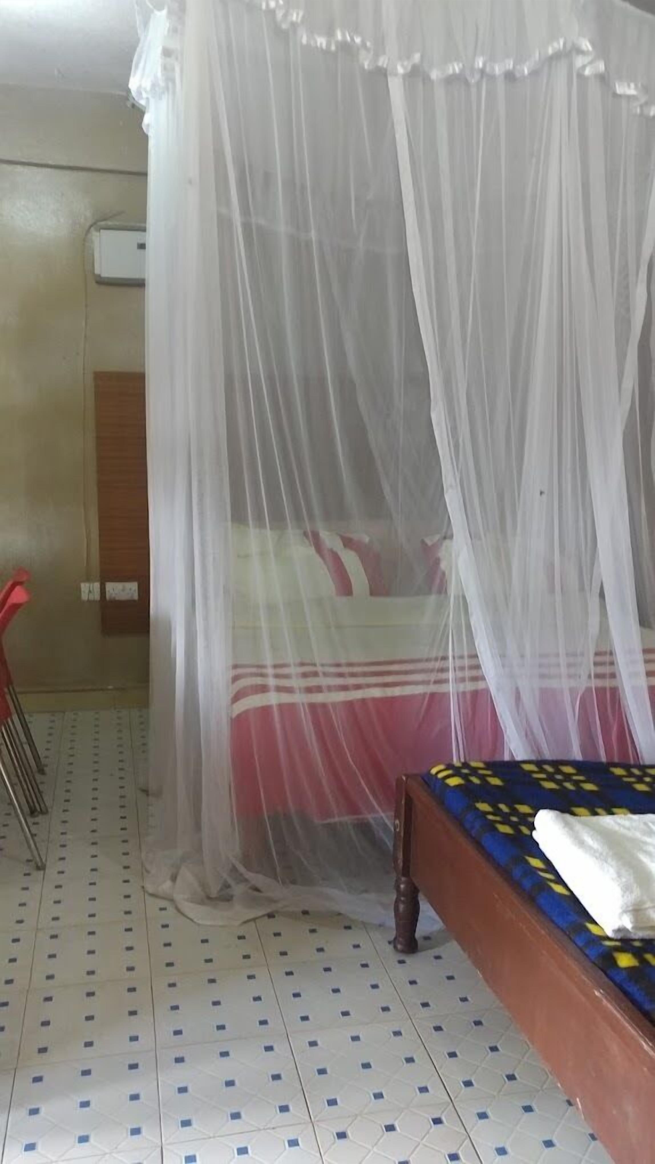A room with a bed under a mosquito net, a wooden headboard, and a tiled floor.