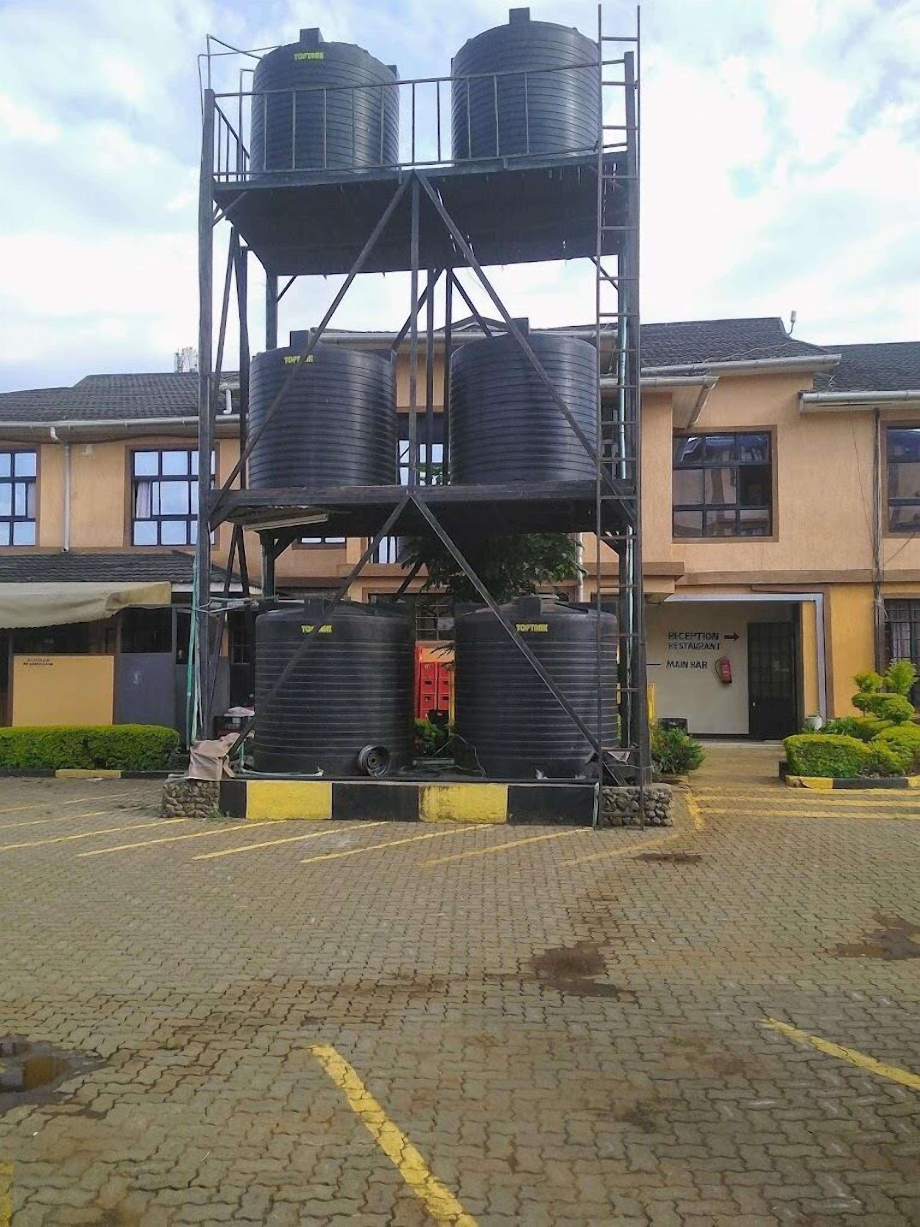 Una estructura de tanque elevado con escaleras metálicas, frente a un edificio que cuenta con recepción y bar principal.