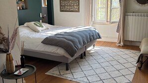 Quarto com cama, mesinha de cabeceira, um objeto decorativo na parede, janela com cortinas e radiador.