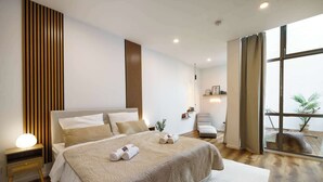 Une chambre moderne avec un grand lit, des tables de chevet, un fauteuil et une vue sur l’extérieur.