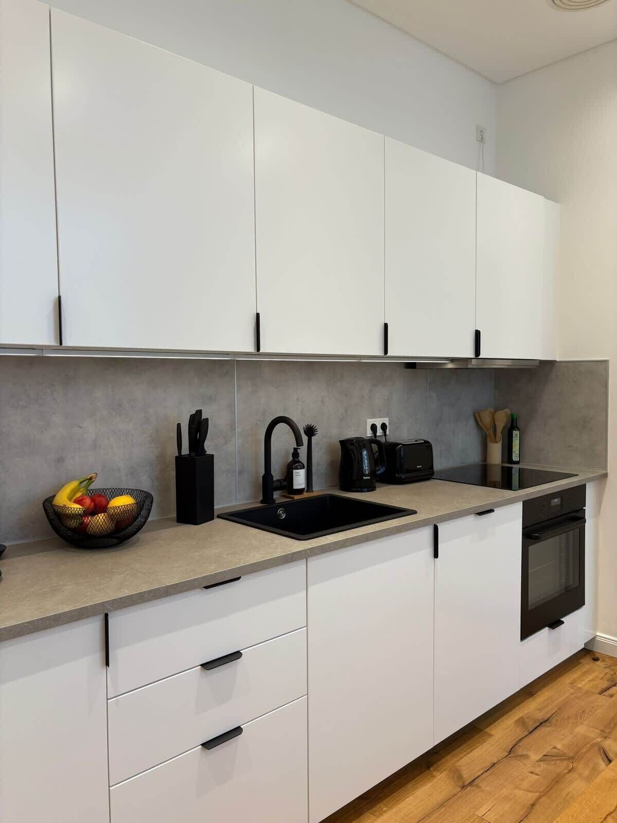 A modern kitchen with white cabinets, a black sink, and a wooden floor.