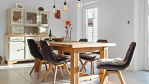 Un comedor con una mesa y sillas de madera, un aparador con puertas de vidrio y lámparas colgantes.