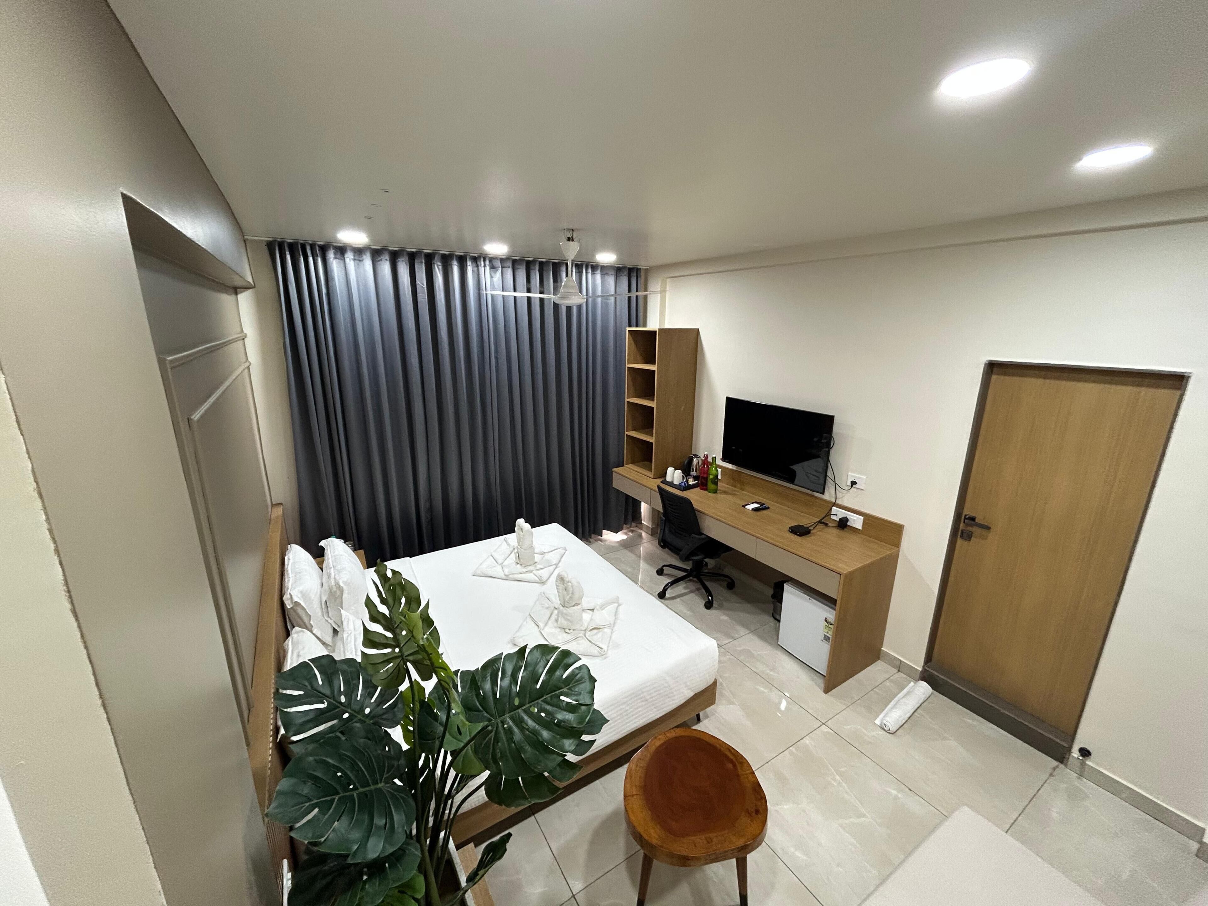A bedroom with a bed, a desk, a chair, a television, a wardrobe, and a potted plant.