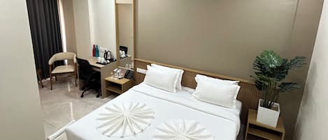 A hotel room with a large bed, a desk with a chair, a ceiling fan, and a potted plant.