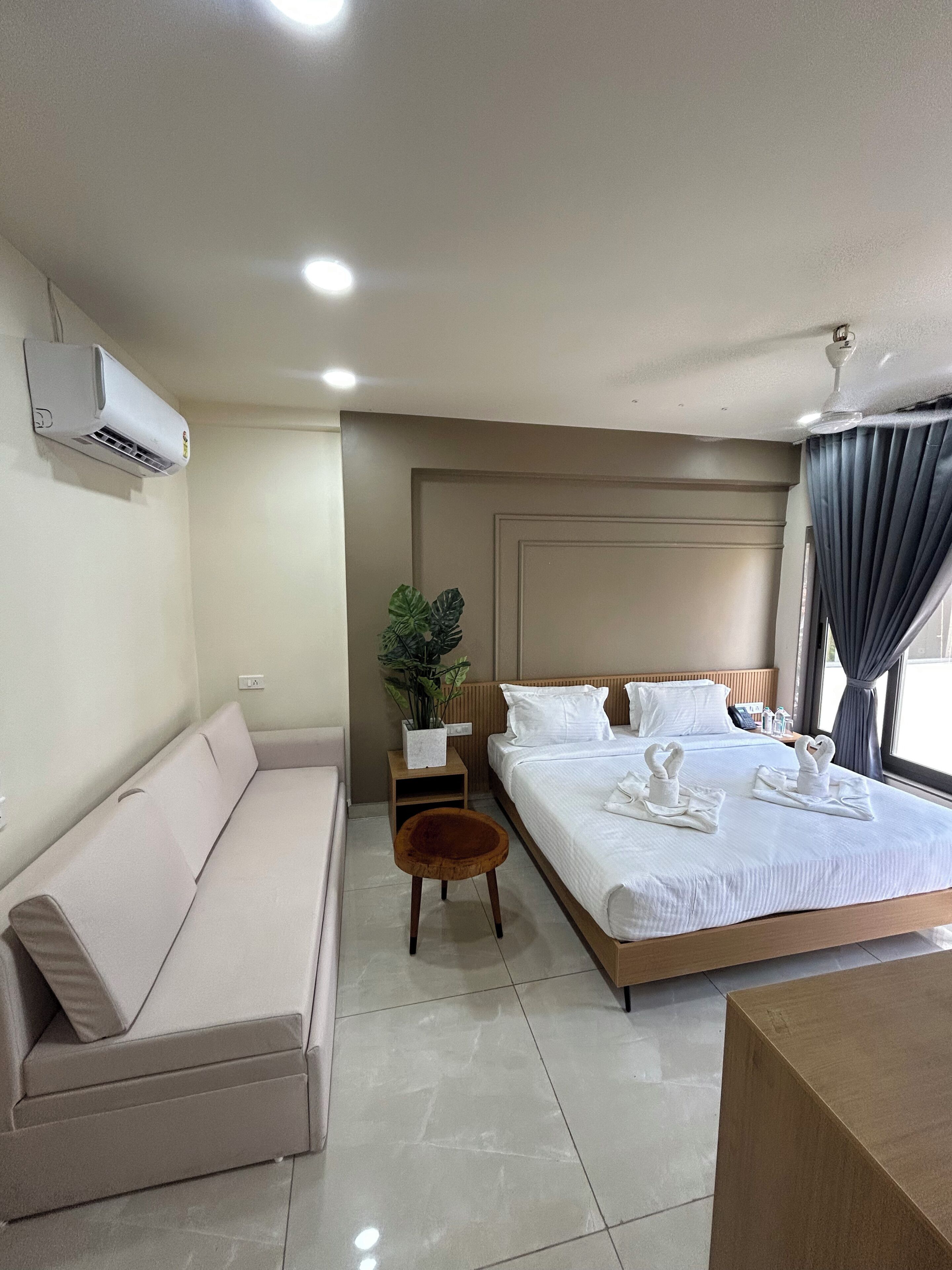 A hotel room with a bed, a sofa, a small table, and a potted plant.