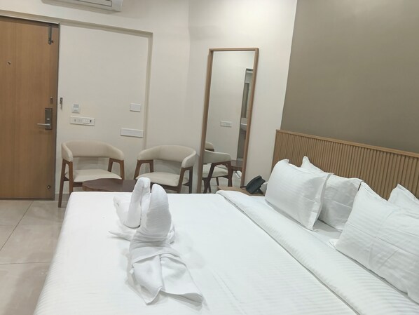 Habitación de hotel con una cama bien hecha, dos sillas, un espejo y un teléfono en la mesita de noche.