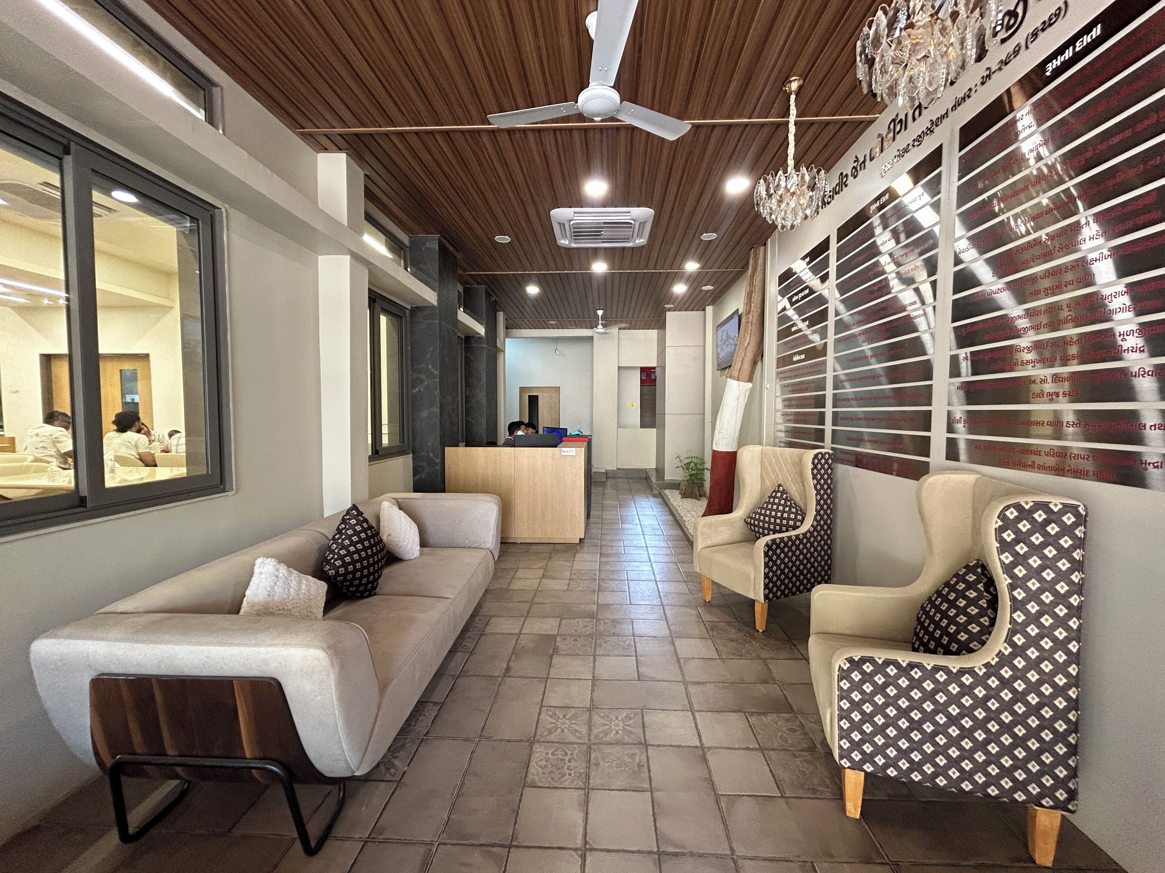 A hotel lobby with a reception desk, seating area with sofas and armchairs, a chandelier, and a ceiling fan.