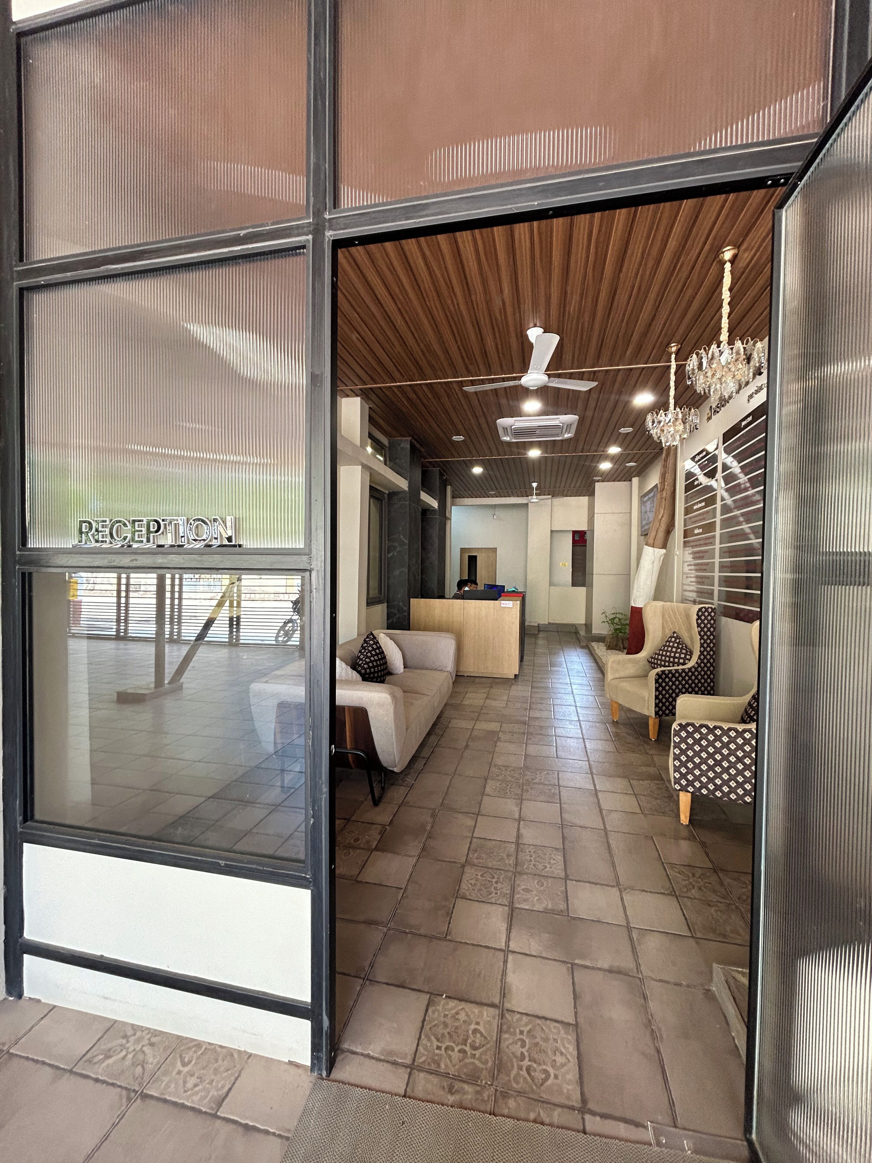 Un área de recepción con un letrero, un mostrador de recepción, un sofá, sillones estampados y un ventilador de techo.
