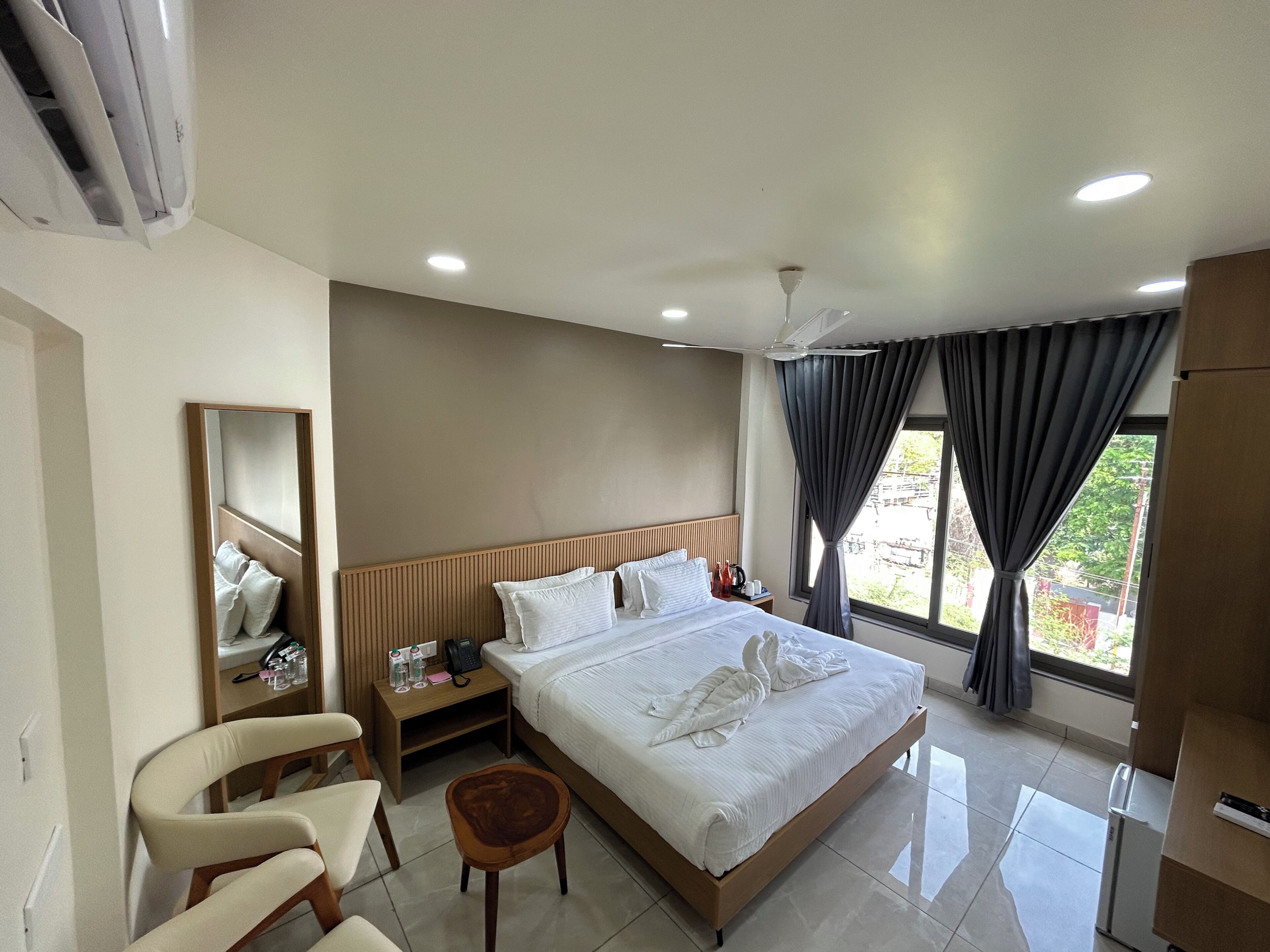 Una habitación de hotel con cama, mesita de noche, silla y un espejo grande.