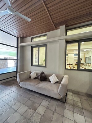 A modern interior with a beige sofa, two windows, and a ceiling fan.