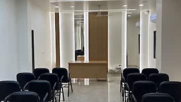 Un salón de conferencias con mostrador de recepción, sillas negras dispuestas en filas, ventilador de techo e iluminación empotrada.