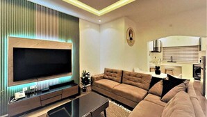 A modern living room with a large flat-screen TV, a sectional sofa, a coffee table, and a built-in entertainment unit. - Quick Stay  (Abuja)