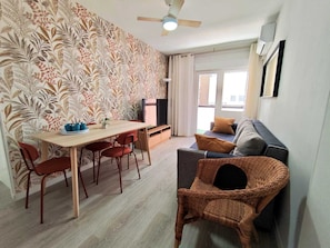 A modern living space with a dining area, a sofa, a TV, and a ceiling fan.