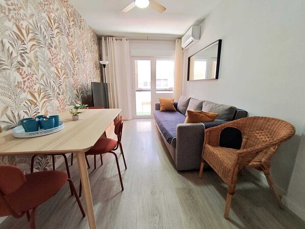 Ein modernes Wohnzimmer mit einer Couch, einem Esstisch mit Stühlen, einem Korbstuhl und einem großen Spiegel.
