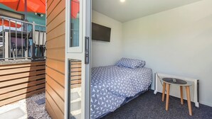 A bedroom with a bed, a small table, a TV on the wall, and a window with blinds. - Casa Verde - Mapua Holiday Home (Mapua)