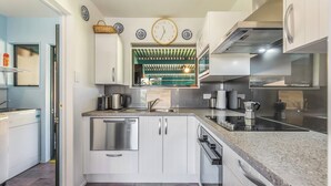 A modern kitchen with white cabinetry, stainless steel appliances, and a green-striped window blind. - Casa Verde - Mapua Holiday Home (Mapua)