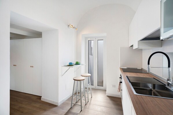 Una cucina moderna con mobili bianchi, un lavello in acciaio inossidabile e due sgabelli da bar.