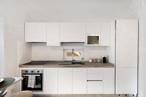 A modern kitchen with white cabinetry, a built-in oven, a stainless steel sink, and a window above the sink. - La Casa Quattrocchi – Tradition and Modern Comfort in Testaccio (Barano D'ischia)