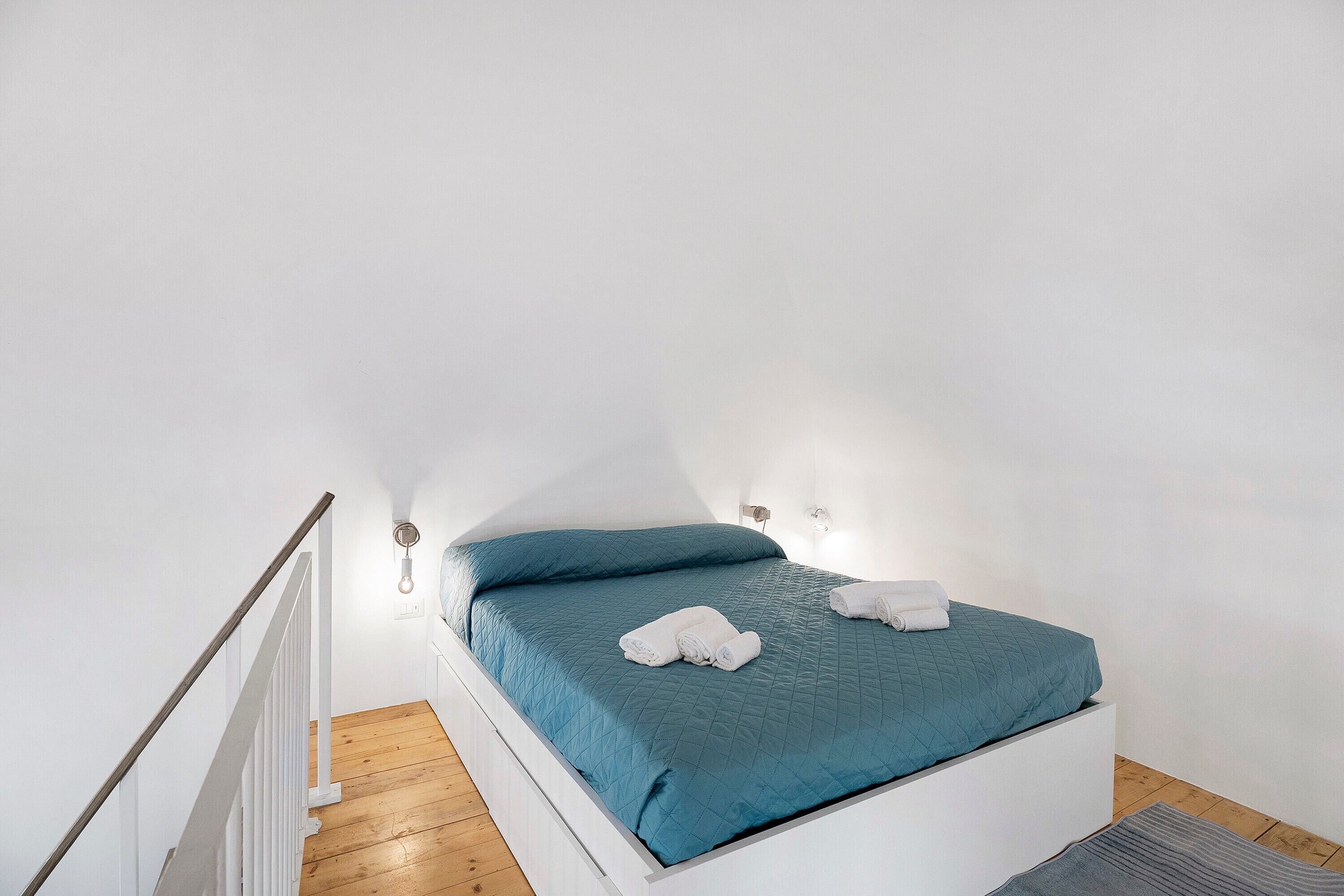 Ein Einzelbett mit blauer Bettdecke, weißen Kissen und zusammengerollten Handtüchern.